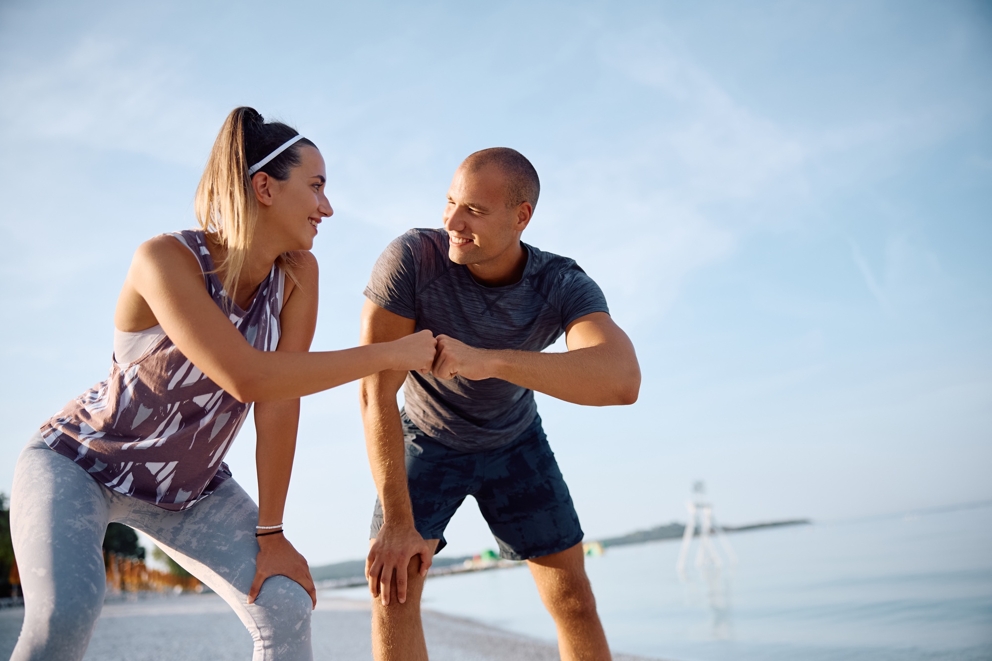 Happy athletic couple fits bumping after running on the beach.